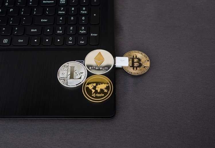 A laptop with replica coins of Litecoin, Ripple, ethereum and Bitcoin on it.