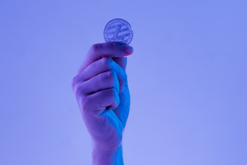 male-hand-with-golden-litecoin-blue-background-min male hand holding a cryptocurrency